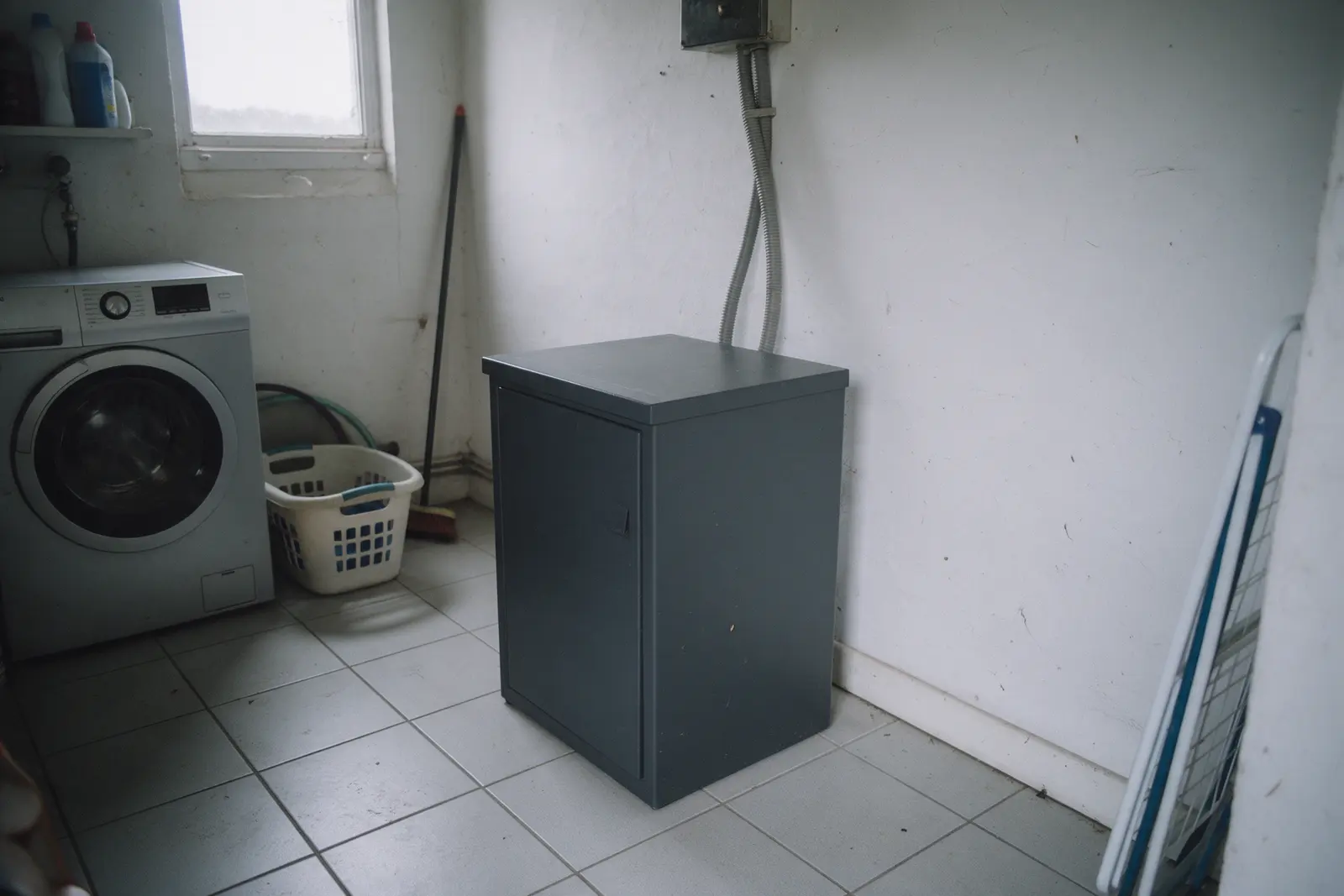 Compacte thuisbatterij in een Vlaamse berging naast een wasmachine, met alledaagse voorwerpen die de schaal tonen