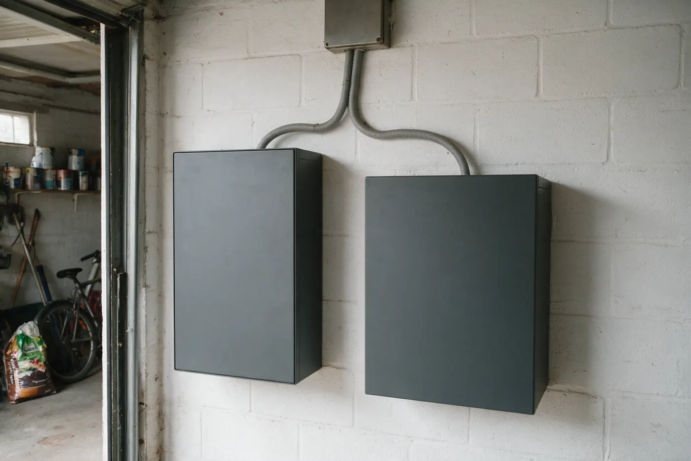 Twee onbedrukte thuisbatterijkasten naast elkaar aan een garagemuur