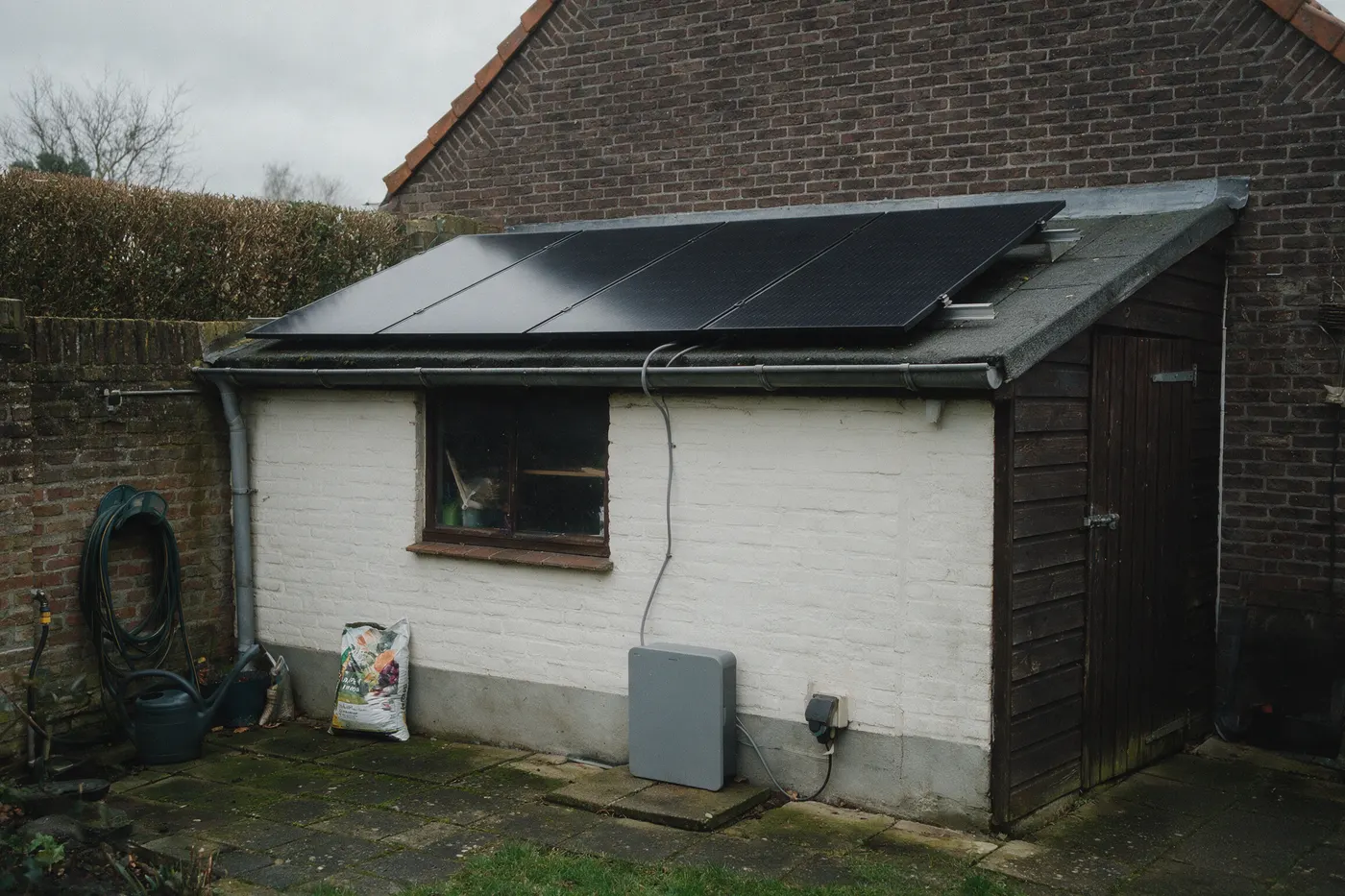 Stekkerzonnepanelen op een tuinhuis in een Vlaamse tuin, met kabel naar een plug-in batterij