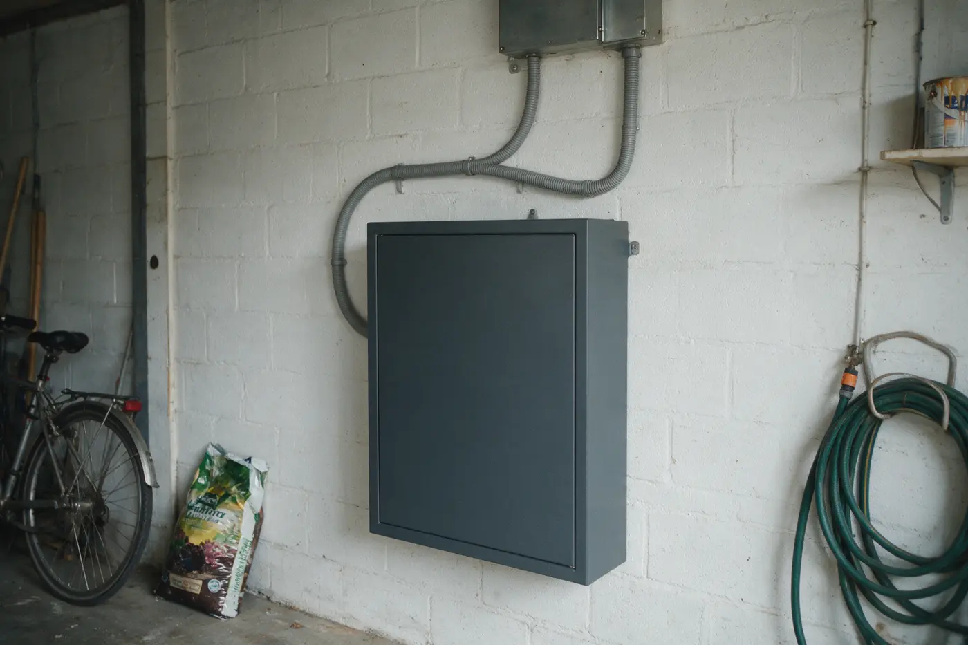 Thuisbatterij aan een garagemuur met bekabeling naar de zekeringkast in een Vlaamse woning