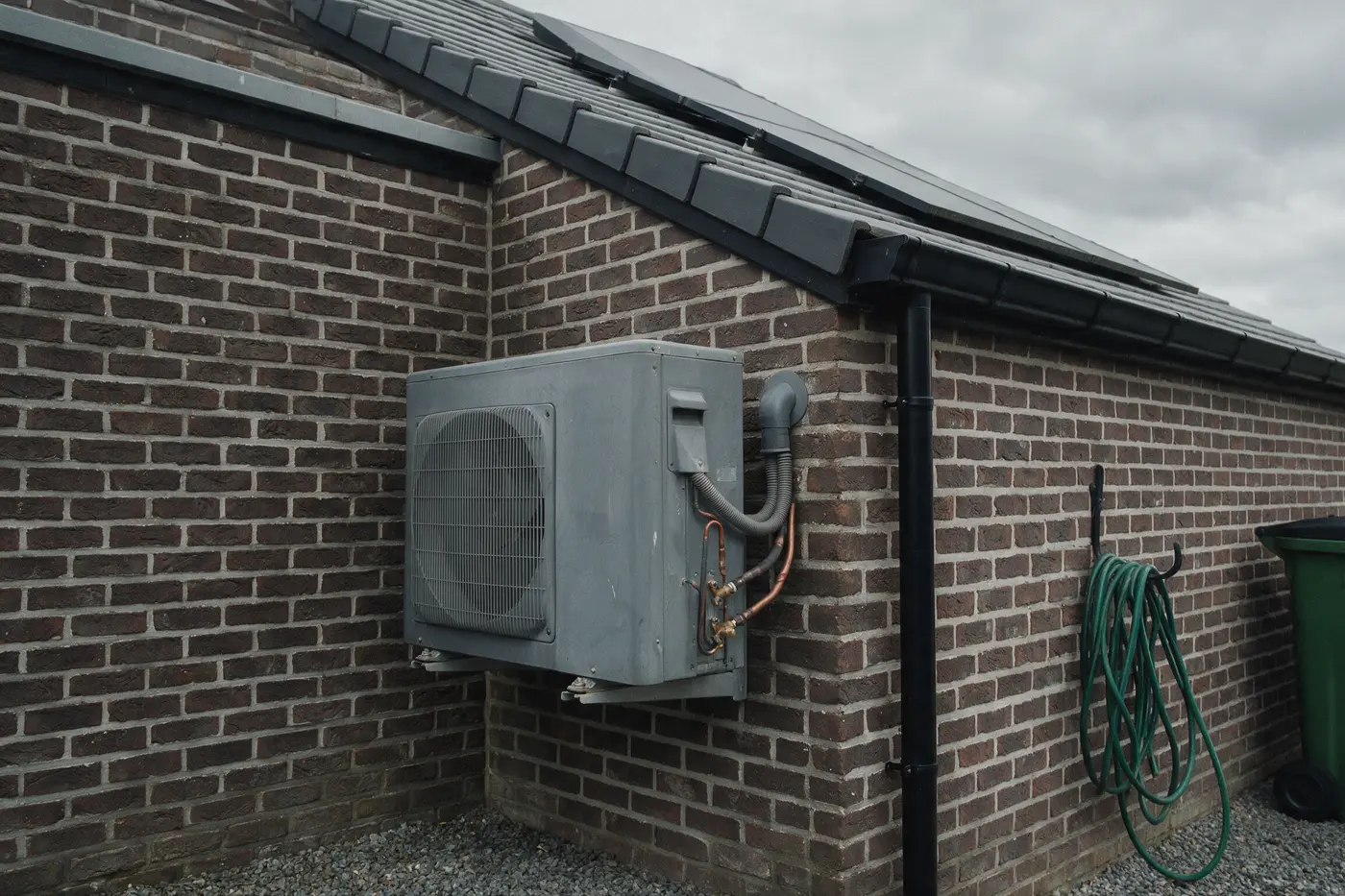 Buitenunit van een airco aan de gevel van een Vlaamse rijwoning met zonnepanelen op het dak