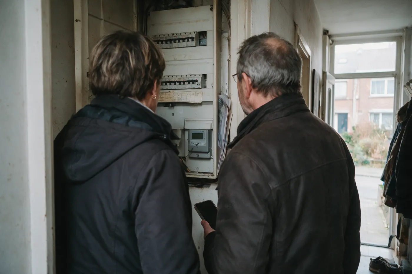 Koppel in de gang bij hun open zekeringkast met digitale meter, telefoon in de hand